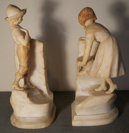 Pair of Circa 1925 Italian Art Deco Enrico Brunelleschi Carved Two-Tone Alabaster Figural Young Boy and Girl by Stone Wall Bookends