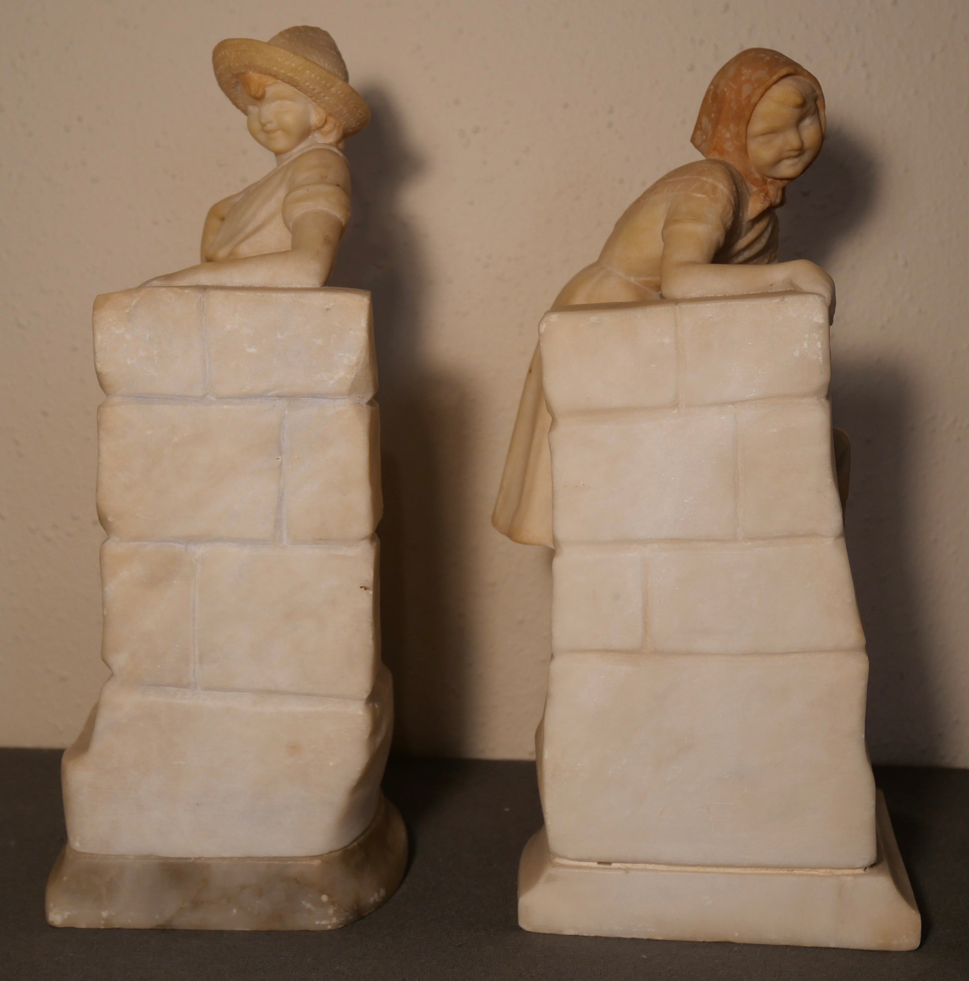 Pair of Circa 1925 Italian Art Deco Enrico Brunelleschi Carved Two-Tone Alabaster Figural Young Boy and Girl by Stone Wall Bookends